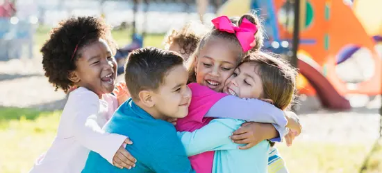A diverse group of happy young children in a group hug at a playground, representing pediatric health and community well-being.