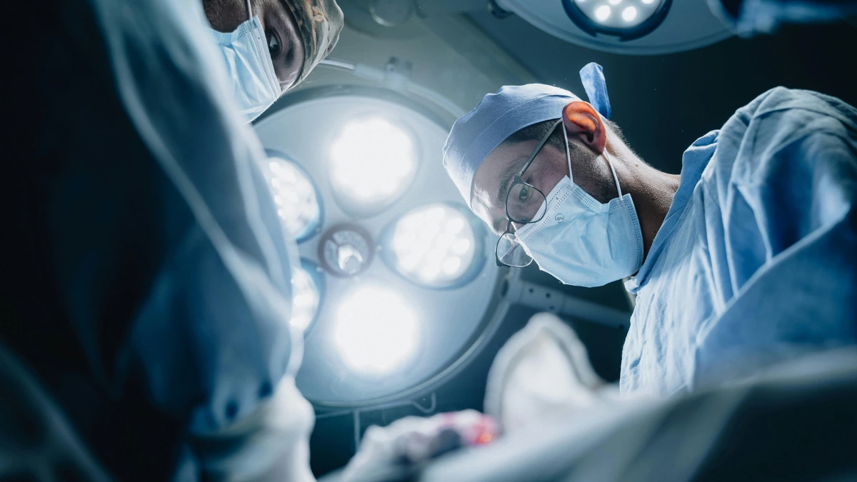 Surgical Team in a Hospital Operating Room Surgeon in glasses and a surgical mask operating under bright lights, with a masked colleague beside him