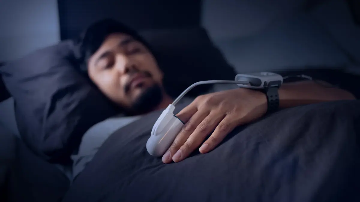 Man sleeping in bed with a fingertip sensor and wrist monitor for a home sleep apnea test