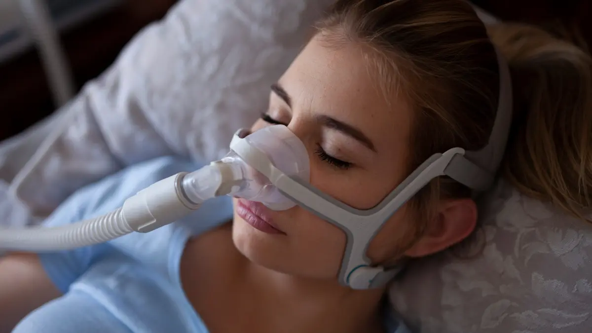 Woman sleeping in bed with a CPAP nasal mask, a common treatment for sleep apnea in women